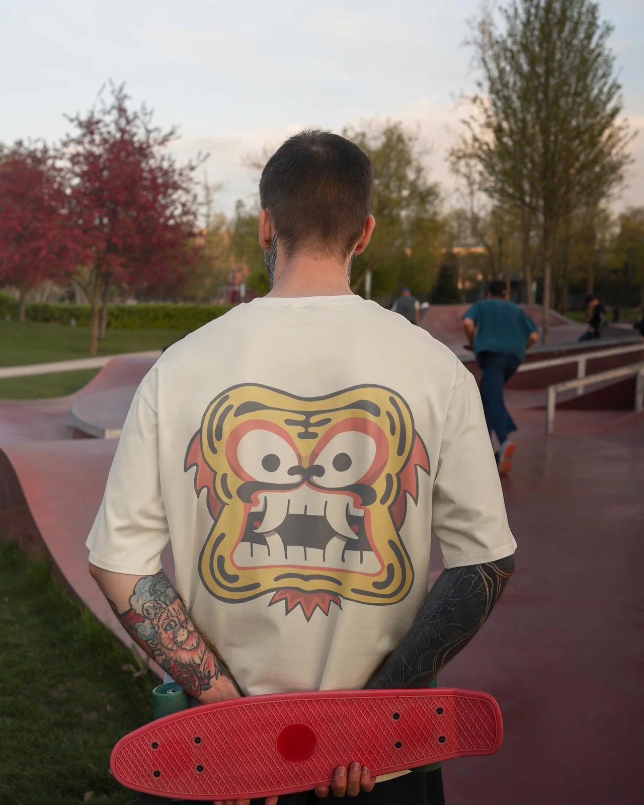 Il visual del drop di giugno 2024: la maschera gialla dai denti aguzzi sul retro di una maglietta chiara, vista da dietro in uno skatepark.